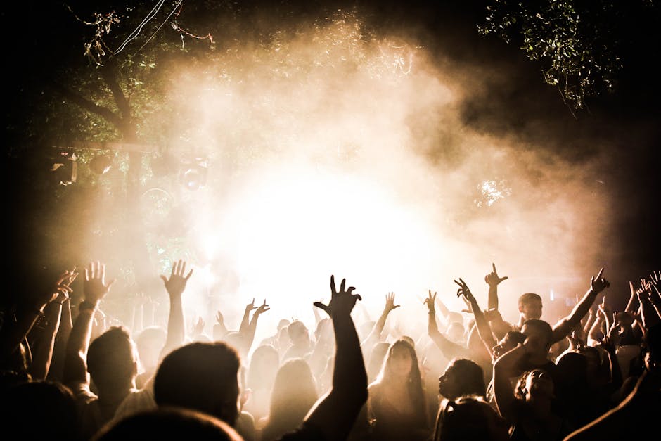 Lively outdoor concert with a crowd raising hands under dramatic lighting.