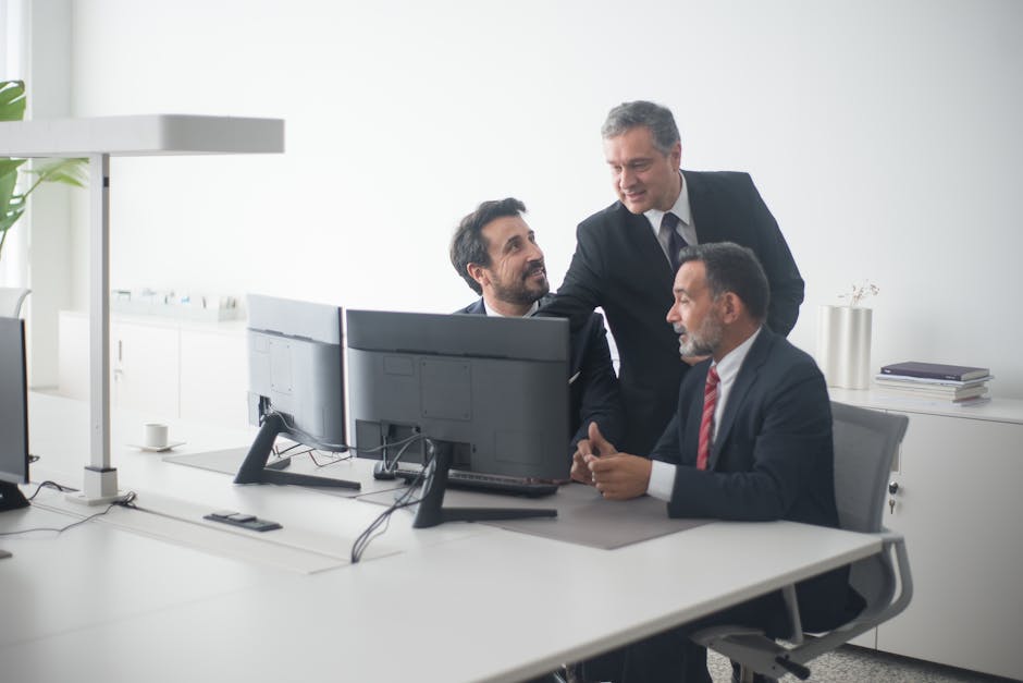 Three business executives in suits collaborating around dual monitors in a modern office setting