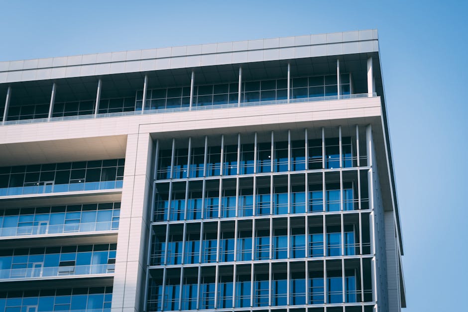A modern high-rise office building with a distinctive glass facade under a clear blue sky